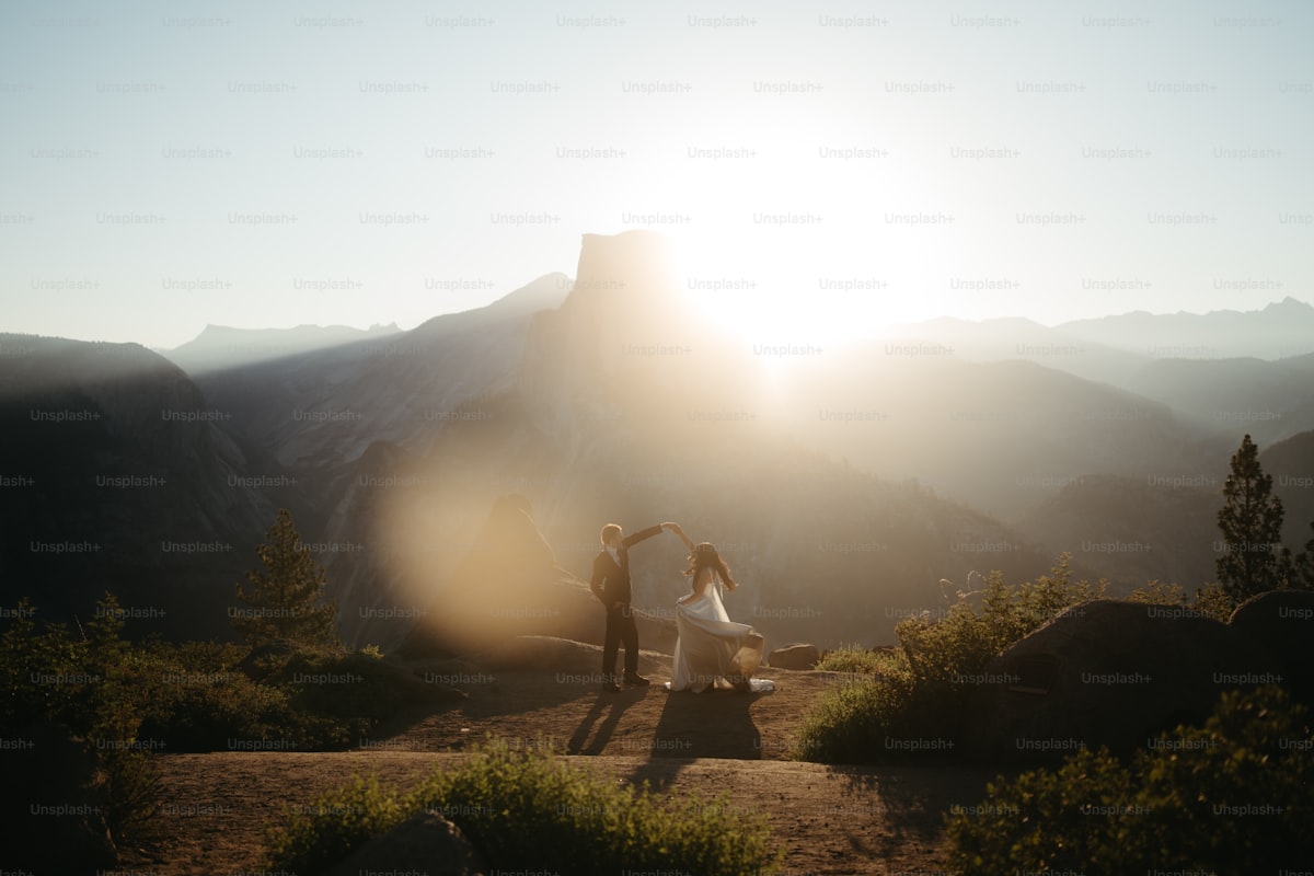 Couple silhouetted against a bright sun in mountainous landscape.