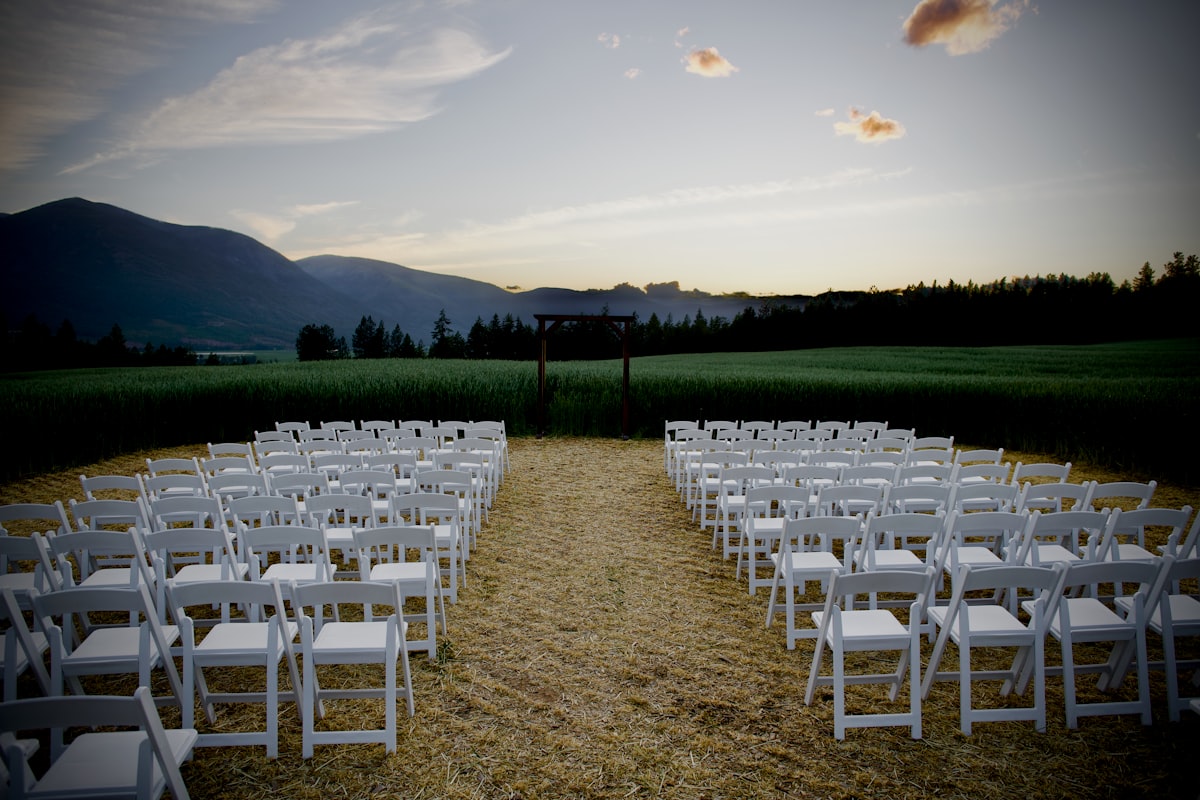 Rows of ceremony chairs facing the mountains at dusk where speaker stands flank the aisle in the Bitterroot Valley