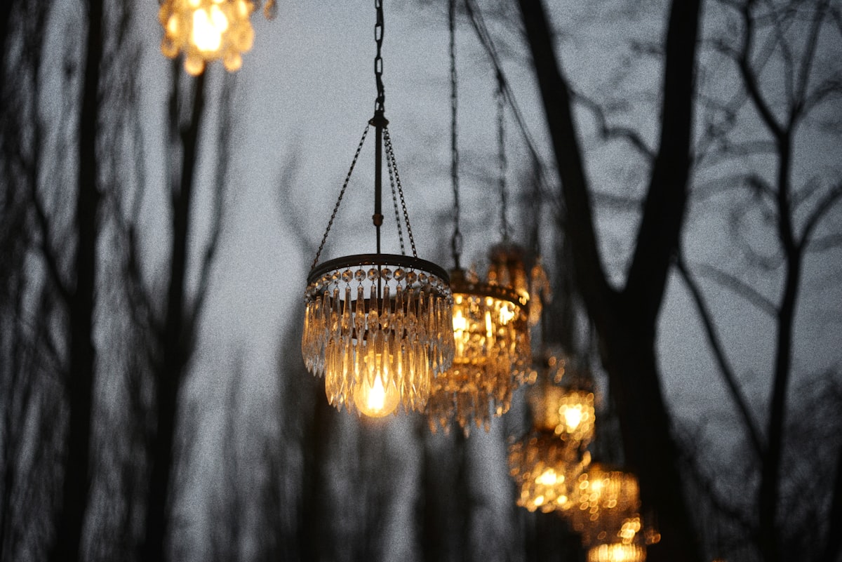 Crystal chandeliers hanging from trees at dusk