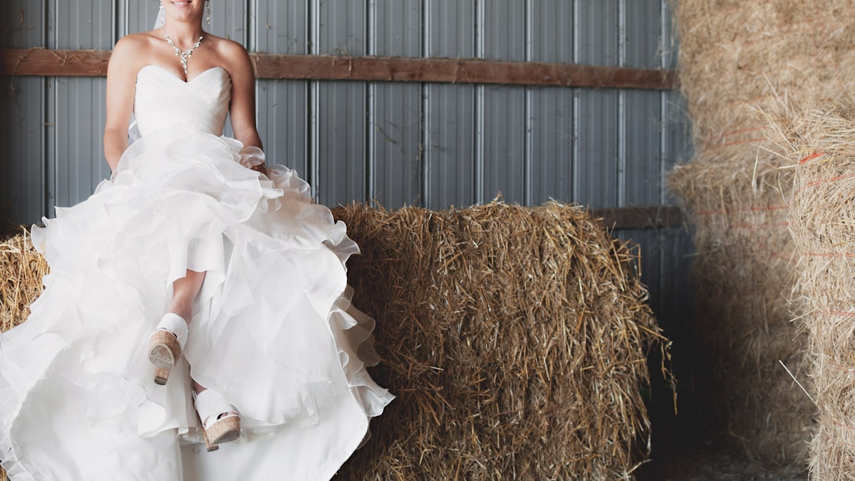 Bride in a flowing gown resting against hay bales at a rustic Montana ranch barn wedding