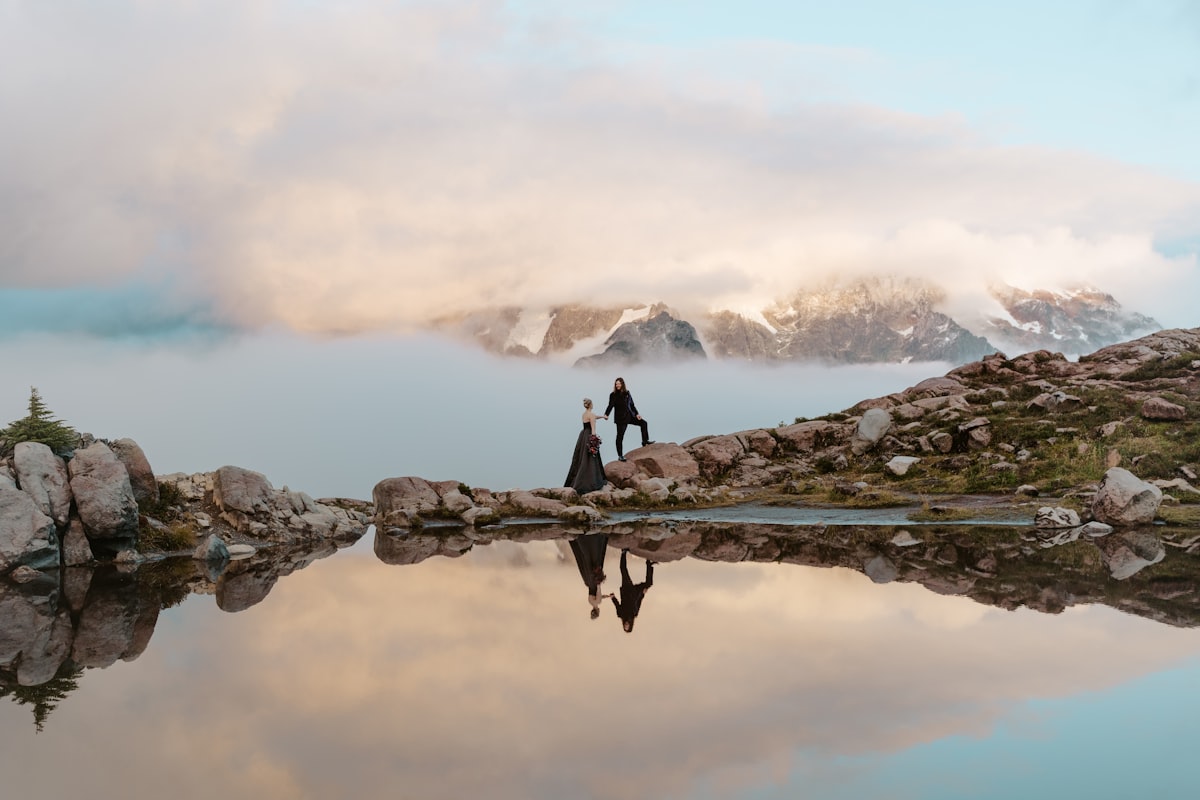 Couple standing on rocks by calm mountain lake reflection