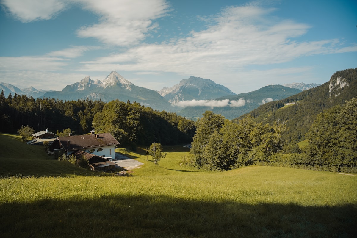 A rural house nestled in a green valley with mountains.